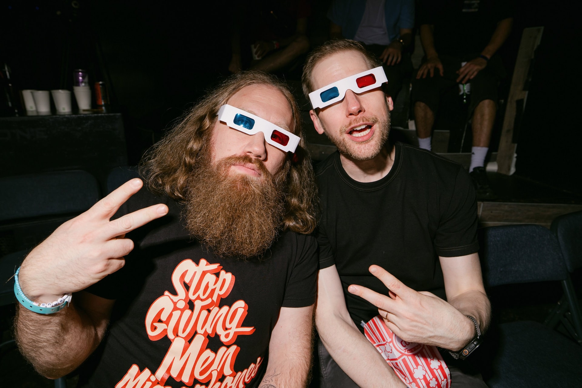 Two cool dudes throwing up peace signs while wearing 3-d glasses. One has a beard, wonderful lustrious beard. Their eyes clearly seen gazing from behind the 3-d glasses (this is Aaron Tarnow). The other dunce-like it is obvious he cannot see out of the 3-d glasses. You cannot see his eyes (this is Jerome Fitzgerald). His face looks like he is saying, “Uh, I cannot see out of these is the picture happening?” The man who cannot see out of the glasses is emitting 1/8th the aura of the bearded man who can. And yet they co-exist. The yin-and-yang of compentence and incomptence.