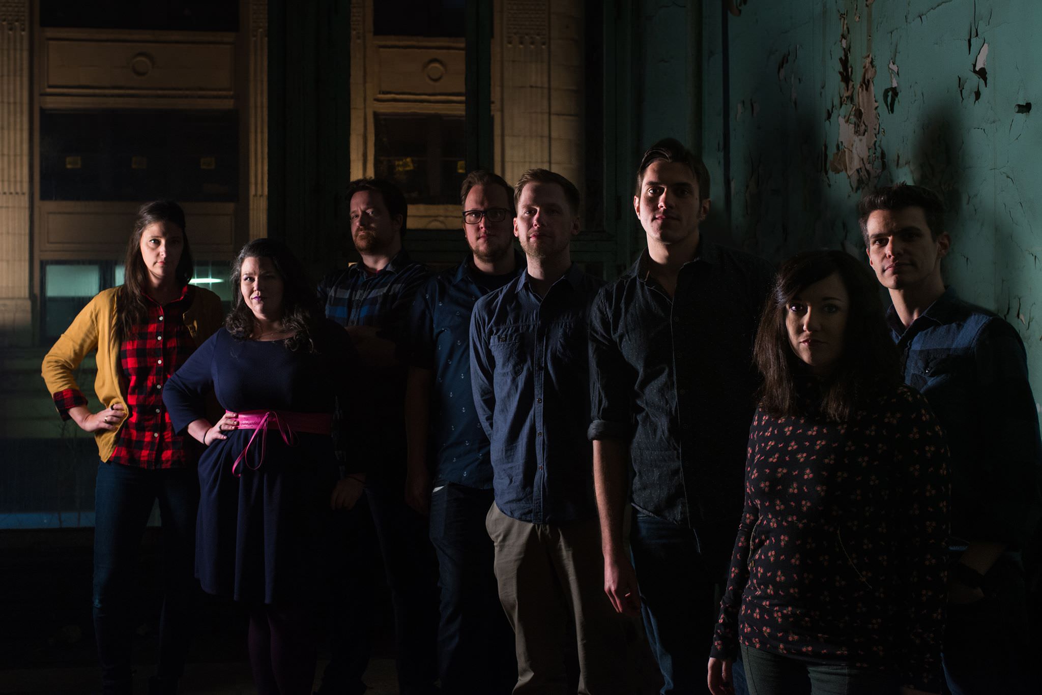 Standing in abandoned building somewhere in Downtown, Pittsburgh is Warp Zone. Dimly lit, this is a classic improv troupe. The wall is peeling, everyone looks ominous. Erica stands with her hands on her hips, in a red flannel and yellow cardigan. Liz in a blue dress with pink belt. John, well, can barely see John, but he is looking debonair I am sure with his red hair and bearded mane. Kyle is wearing glasses dead center, looking dead into the camera, with his dead eyes. Jerome stands with his hands behind him in a blue oxford and khakis. Brett is wearing the same, but with rolled up sleeves and his well-coiffed hair. Abby stands foreground with an all-over print shirt and side bang. Mike rounds out the crew (and shout out to Mike who did this whole photo shoot).